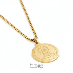 Gold necklace with a round pendant on a white background, featuring the brand 'Blumra'.